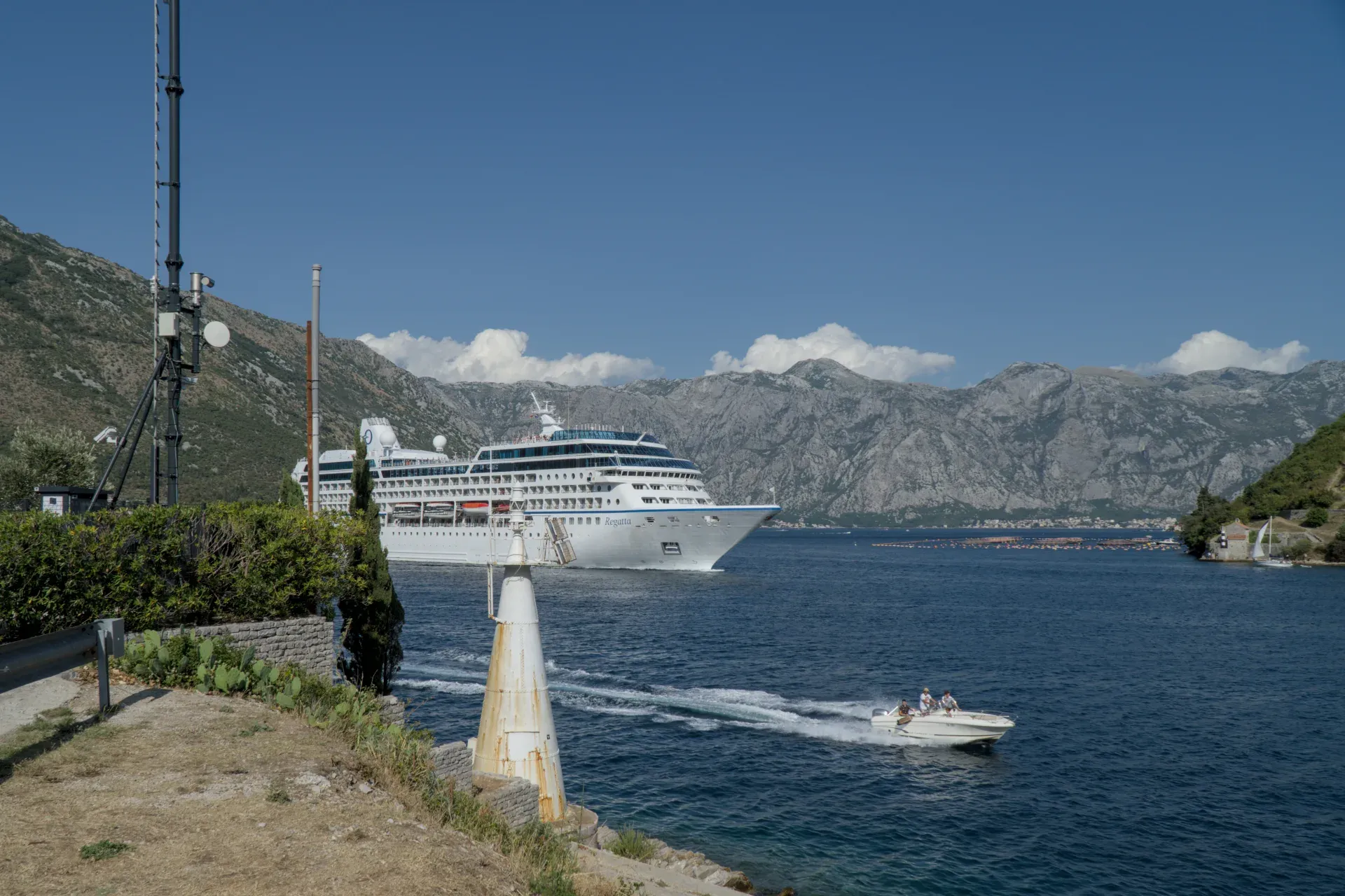 A large cruise ship exits the Bay of Kotor, Montenegro, with smaller boats in the foreground.