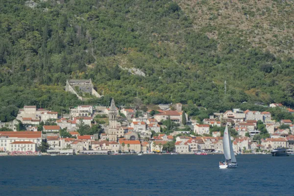 View of Perast in Kotor Bay, featuring a sailboat, with green hills in the background.