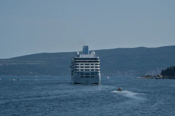 A cruise ship leaves Kotor Bay, surrounded by deep blue waters and lush green hills.