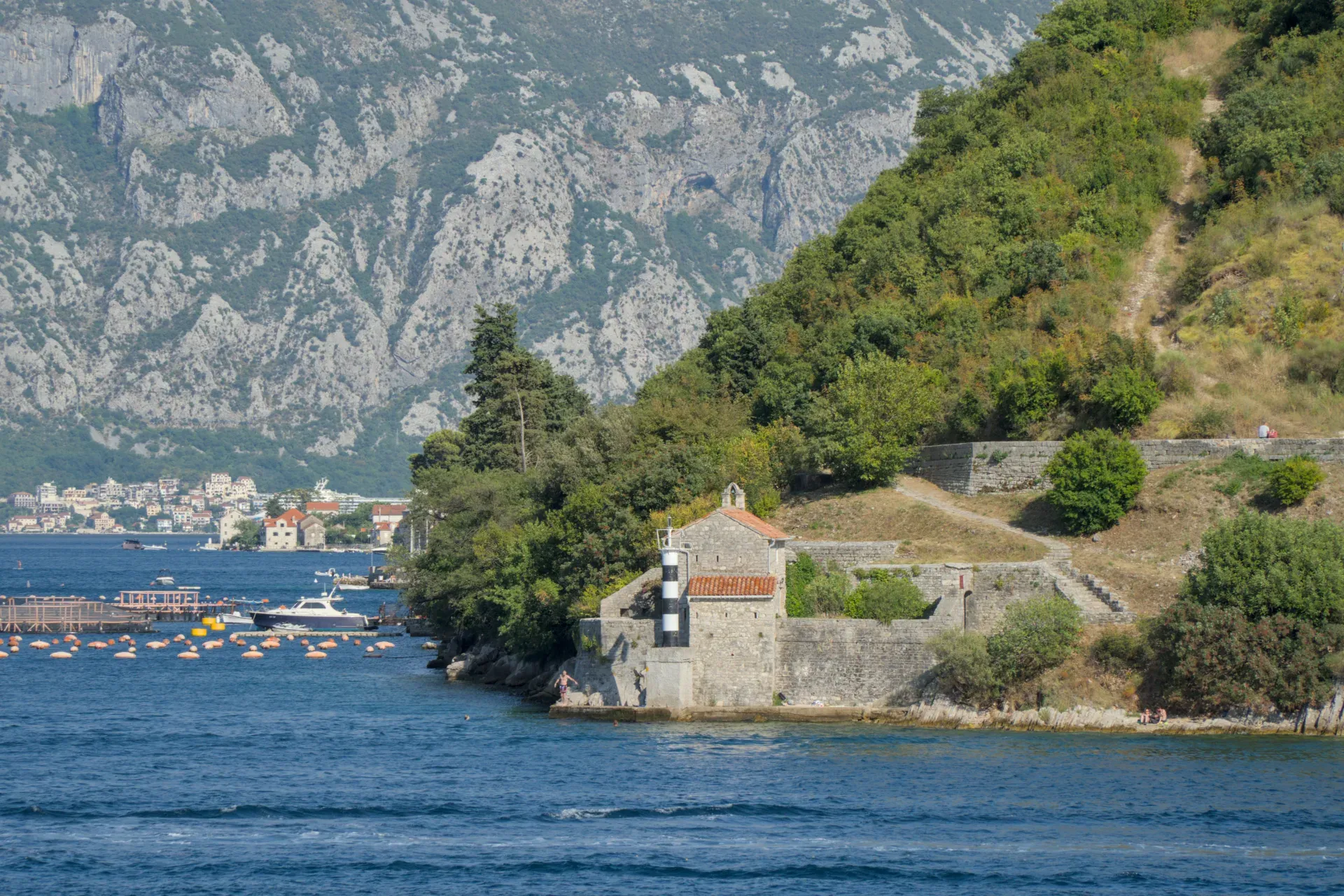 Une petite chapelle en pierre avec un phare rayé noir et blanc sur la côte, face aux montagnes et à l'eau bleue à Kotor.