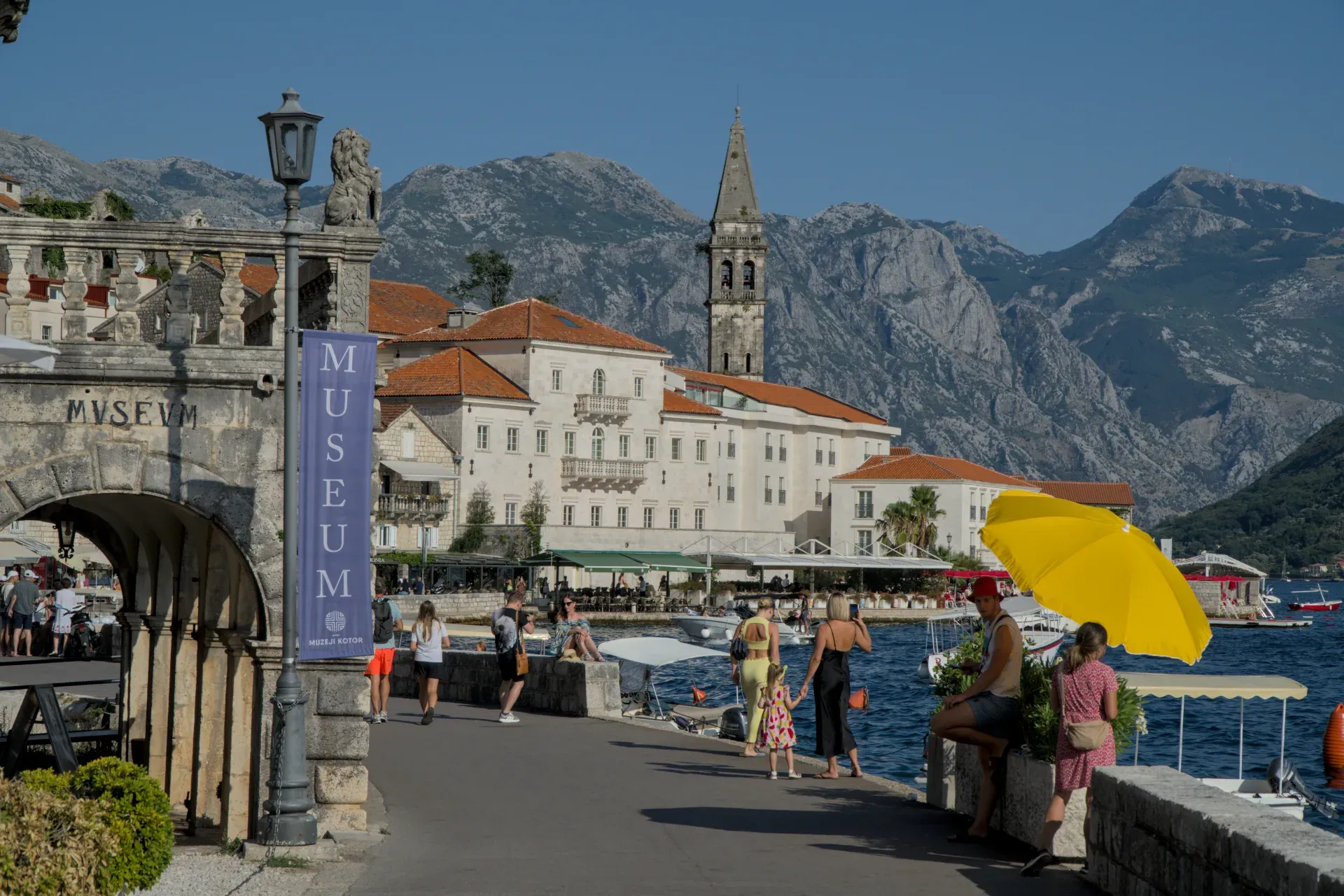Perast promenade with historic buildings and mountains in the background.