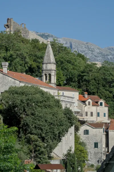 Fine art photograph of Perast, Montenegro, featuring stone buildings, a bell tower, and a mountainous background.