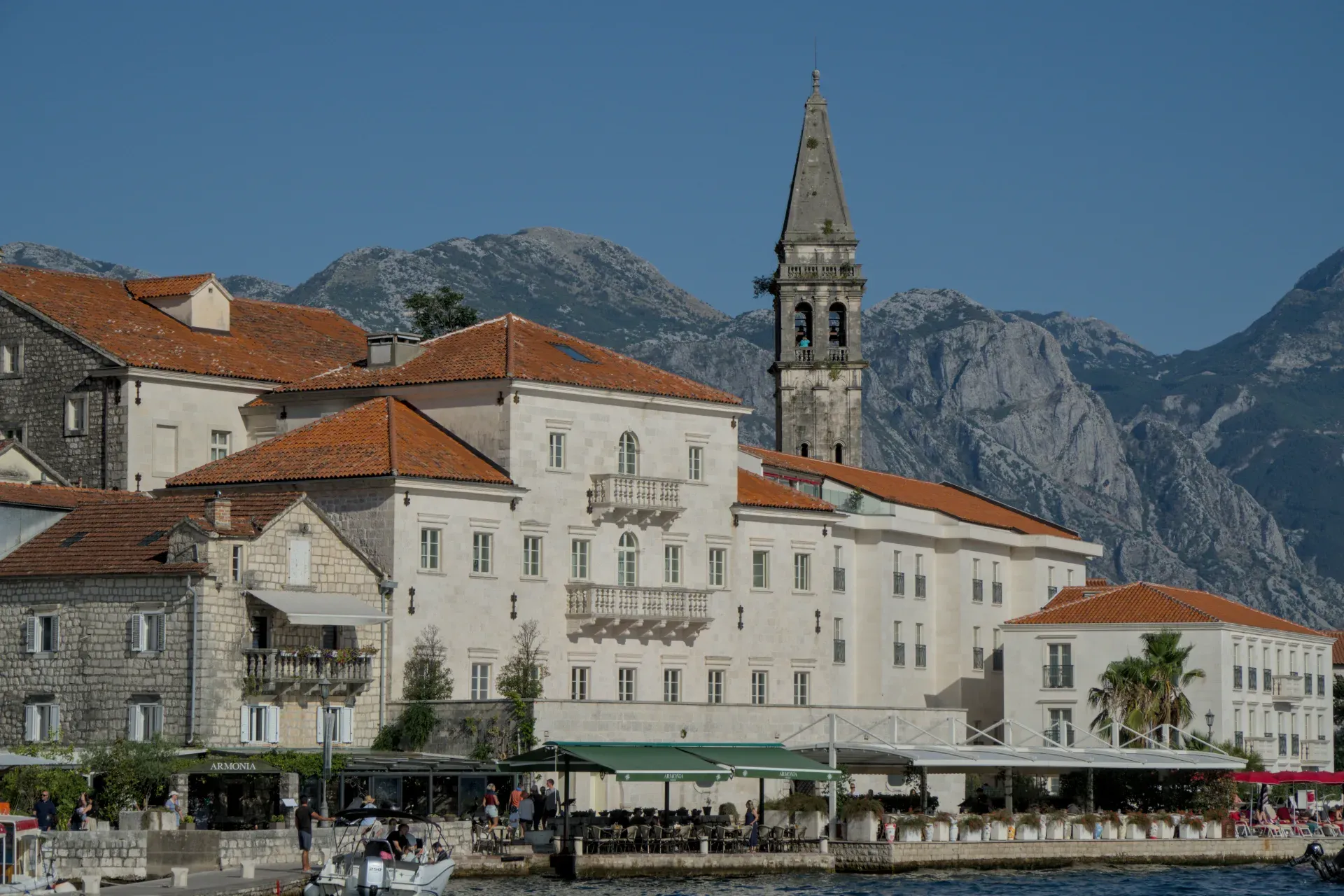 La pintoresca ciudad de Perast en Montenegro al atardecer, con sus edificios históricos y campanario ante un telón de fondo montañoso.