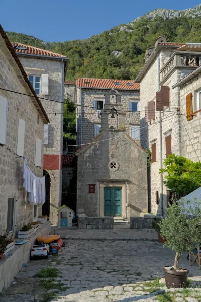 A 'street study in Perast' showing a stone church and buildings in a sunny square in Kotor, Montenegro.