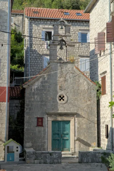The stone Church of St. John the Baptist in Perast, Montenegro, featuring a striking turquoise door and bell tower.
