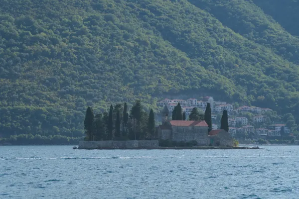 The St. George Monastery on an island in Perast, Montenegro, with lush greenery in the background and calm water in the foreground.