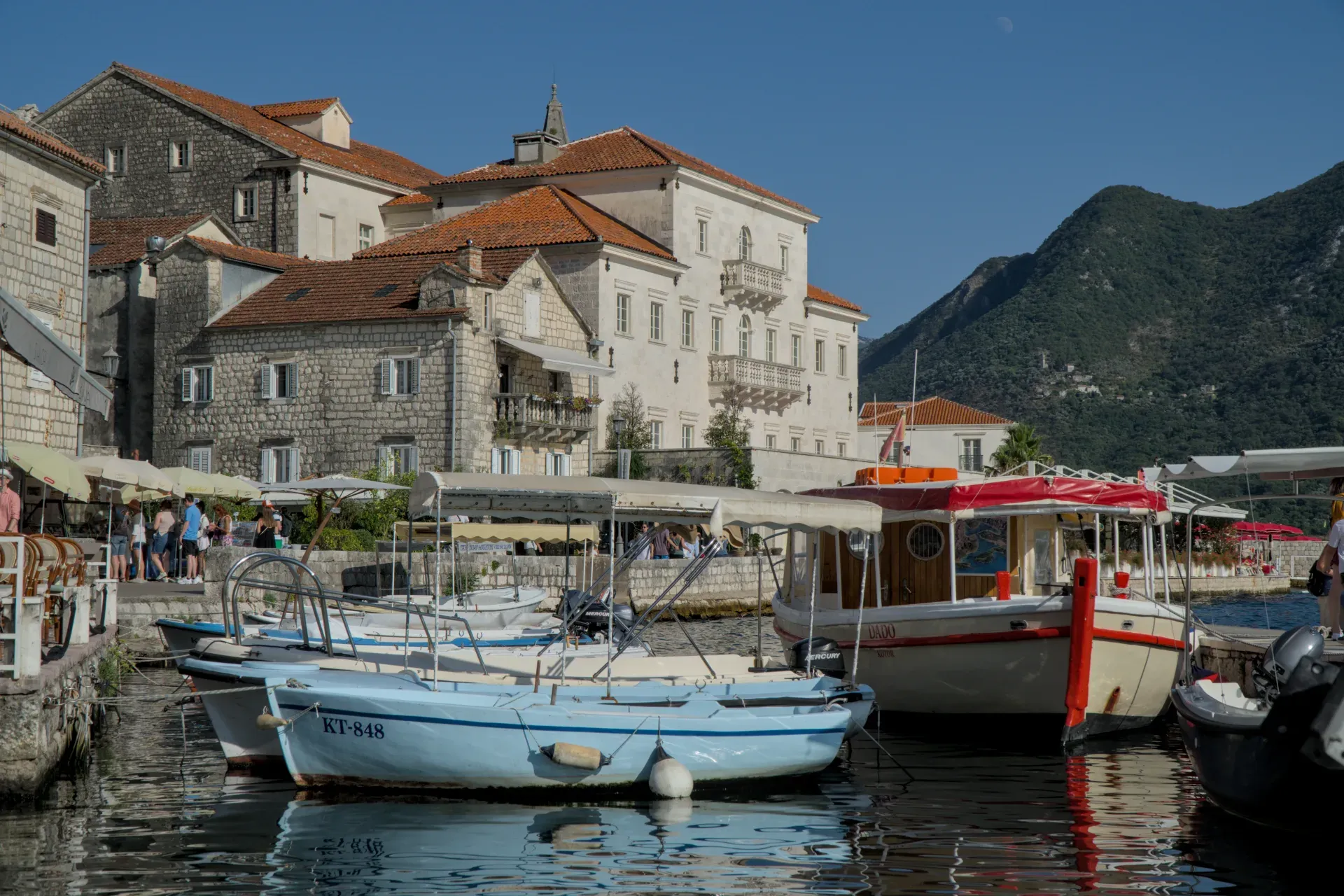 Boot vor historischer Architektur in Perast, Montenegro, bei strahlendem Sonnenschein.