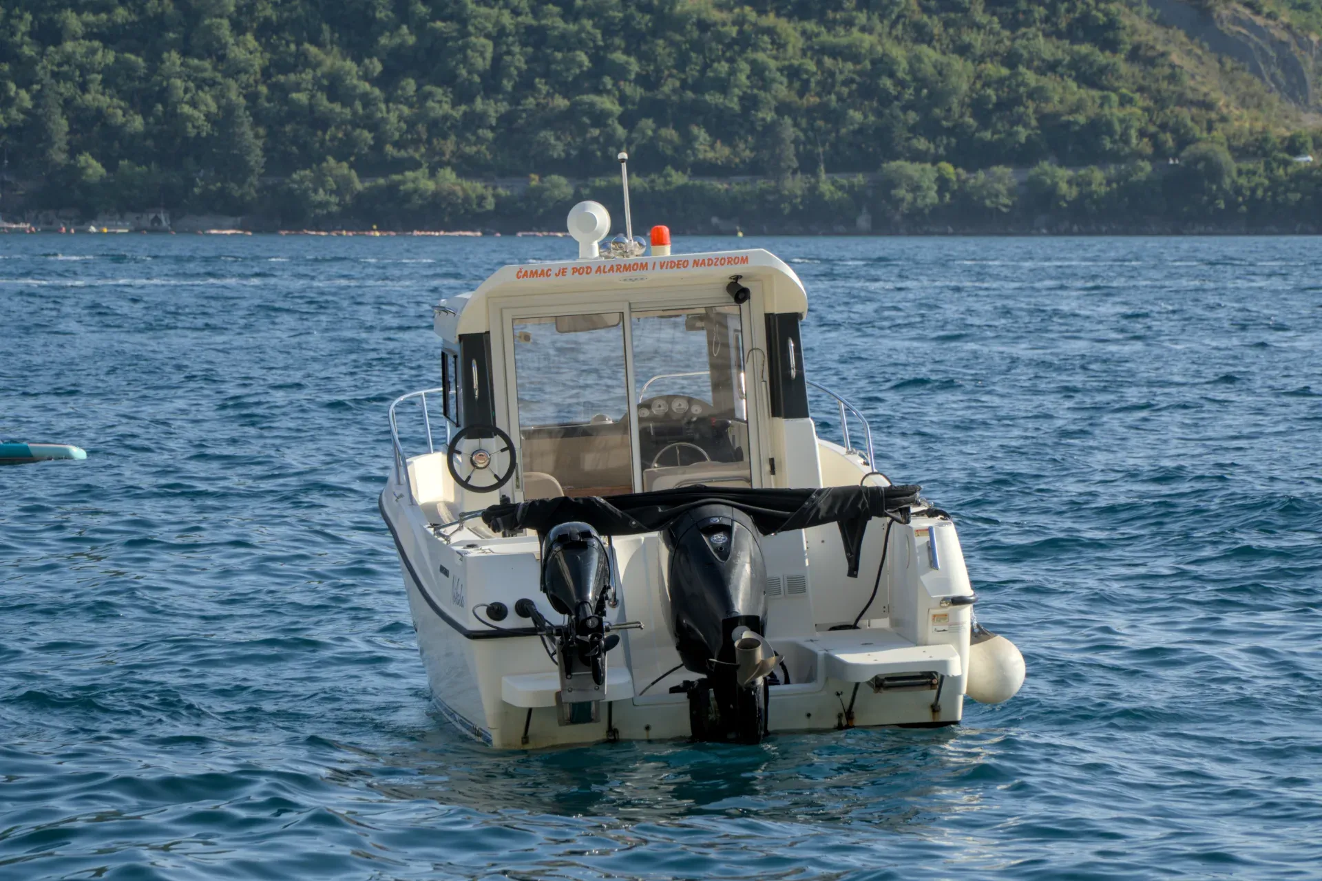 A boat waits for tourists in the calm waters of Perast, Montenegro, with green hills in the background.
