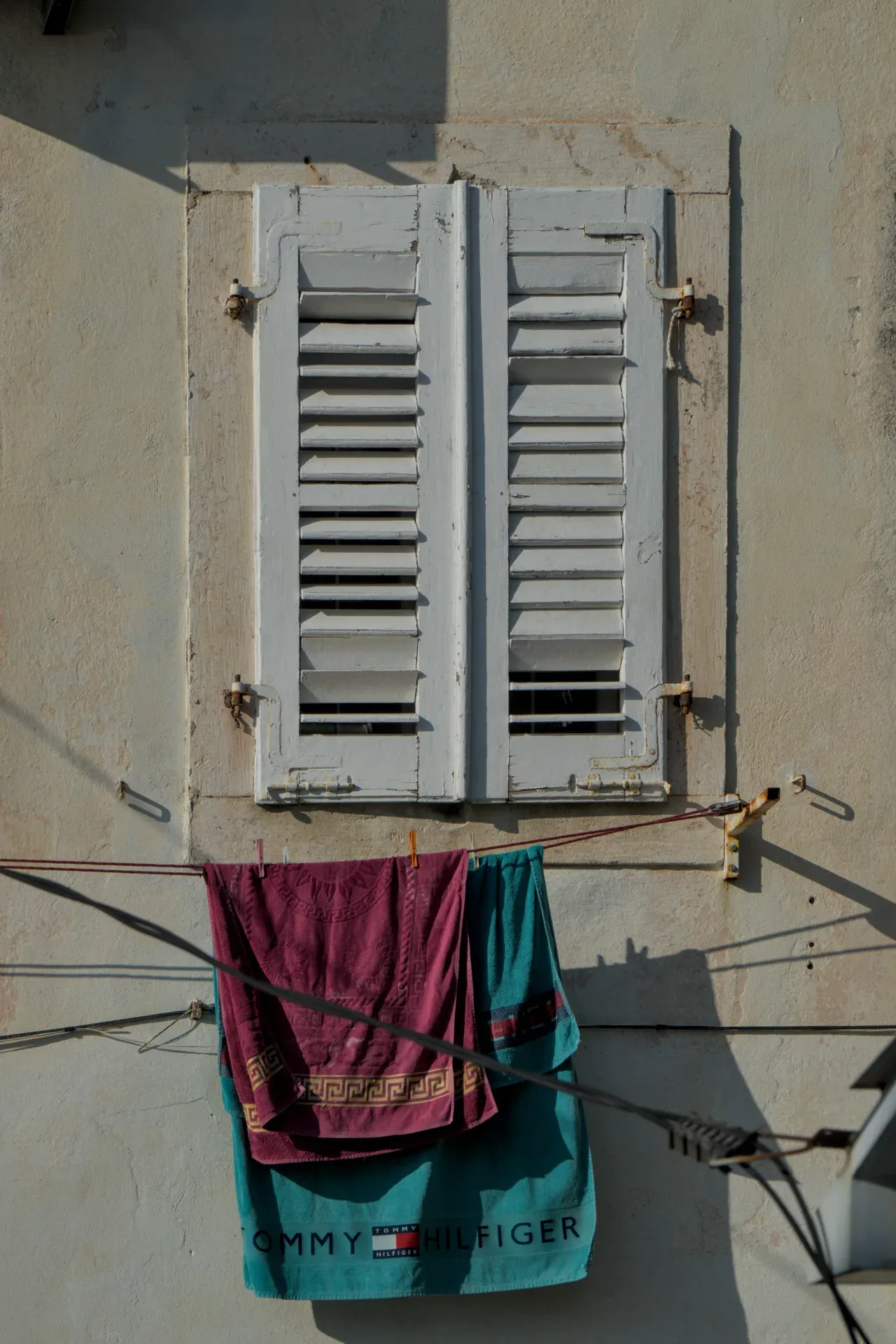 Una ventana con persianas de madera blancas en Perast, Montenegro, con ropa colorida colgando de un tendedero.