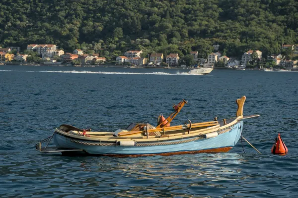A light blue boat drifts on the calm waters of the Bay of Kotor near Perast, Montenegro.