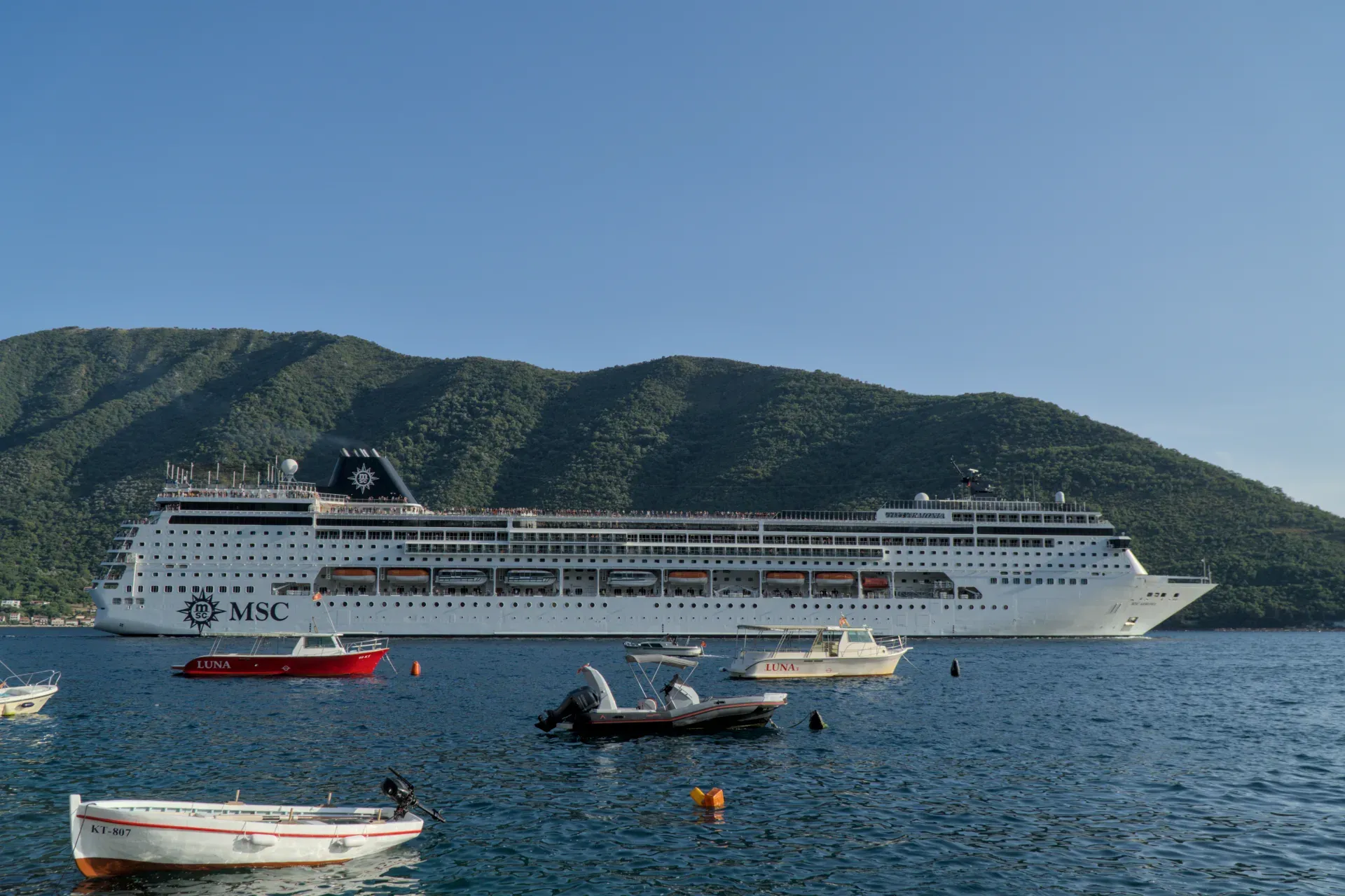 A large cruise ship leaving the Bay of Kotor with mountains in the background.