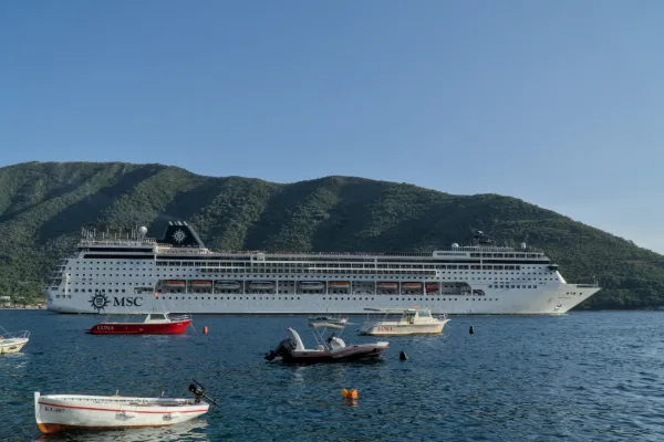 A large cruise ship leaving the Bay of Kotor with mountains in the background.