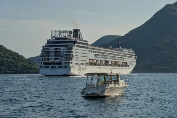 A cruise ship leaves the Bay of Kotor, Montenegro, with a smaller boat in the foreground.