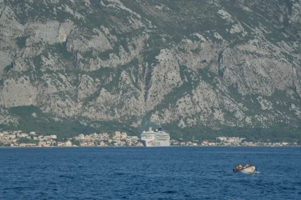 A cruise ship and small boats on the sea in front of the town of Kotor with its houses and the mountains behind.