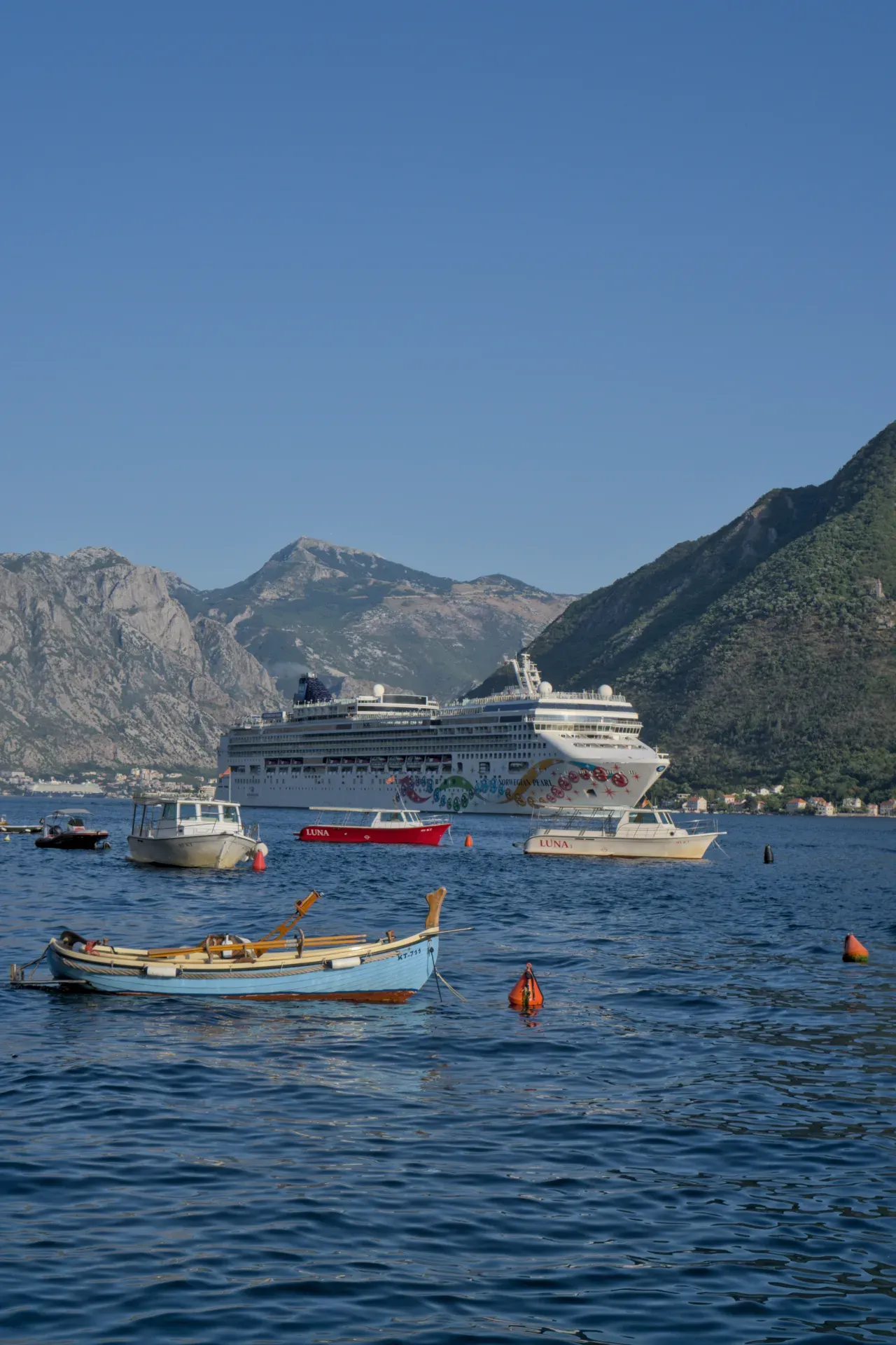 Un grand paquebot quitte la baie de Kotor par Perast, avec de plus petits bateaux au premier plan.