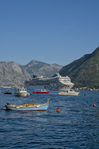 A large cruise ship leaves the Bay of Kotor through Perast, with smaller boats in the foreground.