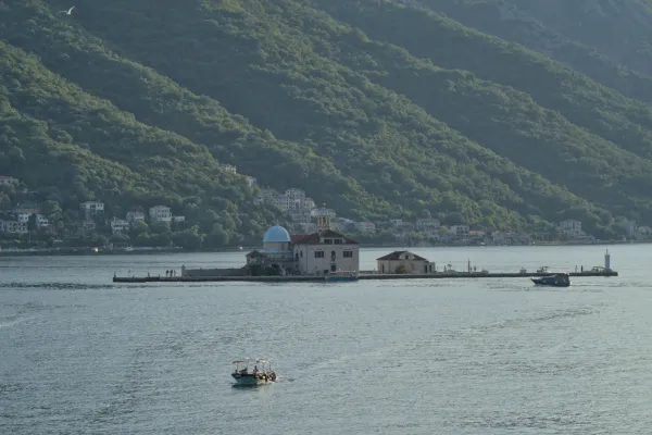 Our Lady of the Rocks island church in Kotor, Montenegro at sunset, with green hills in the background.