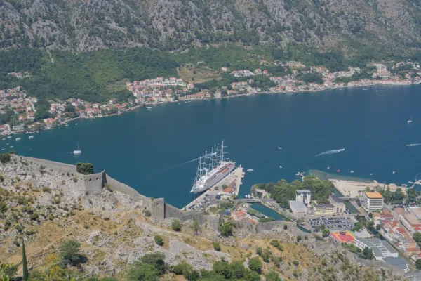 A grand sailboat is moored at the dock in Kotor bay, Montenegro, with ancient fortifications in the foreground.