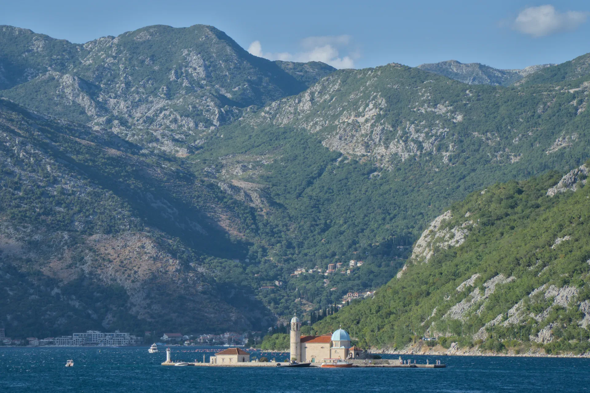 The "Gospa od Škrpjela" church on an island in the Bay of Kotor, Montenegro, set against a mountain backdrop.