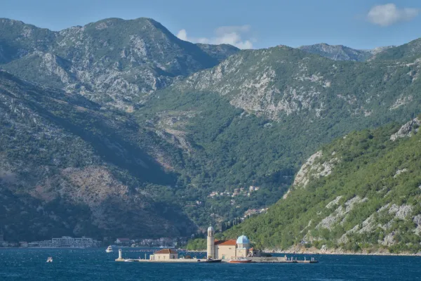 The "Gospa od Škrpjela" church on an island in the Bay of Kotor, Montenegro, set against a mountain backdrop.