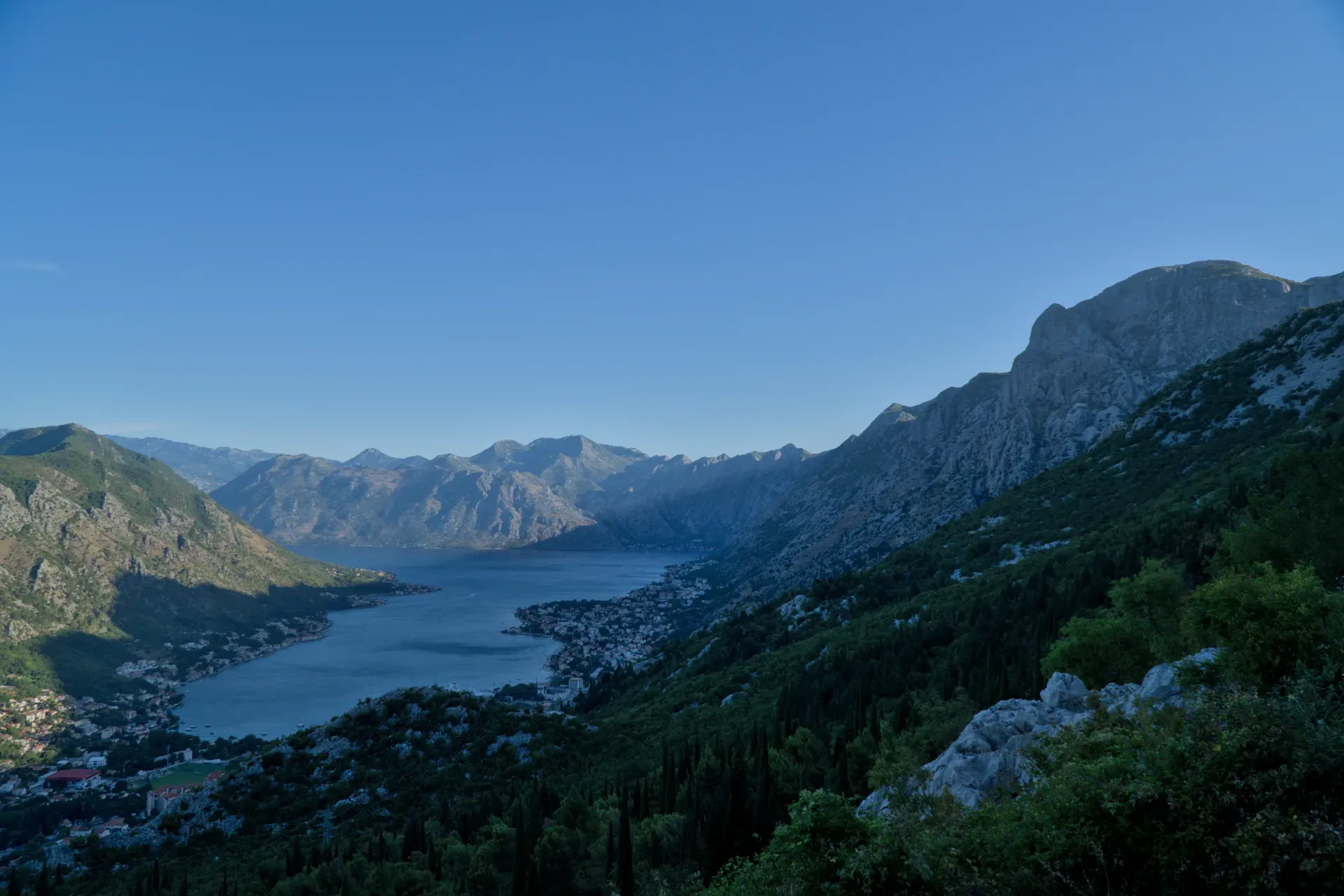Kotor Bay before sunrise, seen from the mountain serpentine road, with calm waters and the awakening town below.