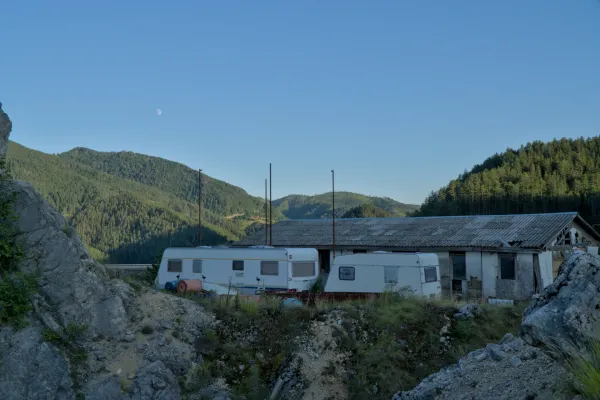 Two caravans rest on rocky ground against forested hills and a clear sky, inspired by Zaovine.