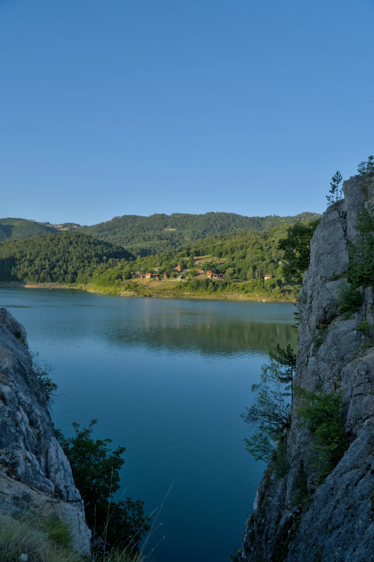 Atardecer en el Lago Zaovine, Serbia, con colinas boscosas y primer plano rocoso.