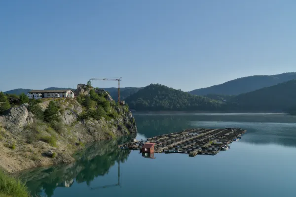 Sunrise at Zaovine Lake, Serbia. Calm water reflects mountains and clear sky with floating structures.