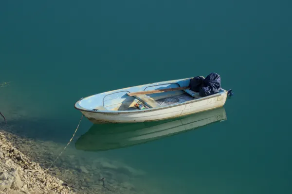 A white rowboat with blue accents floats tied on the calm, turquoise waters of Lake Zaozisko at sunrise.