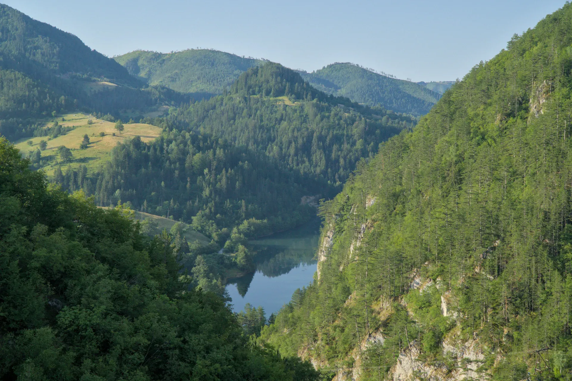 Scenic overlook from Lazic Dam towards Spajic lake, framed by lush mountain forests and meadows.