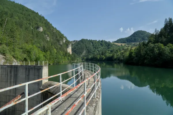 The Spajići Lake Dam in Serbia, featuring its curved walkway and surrounding lush green mountain landscape.