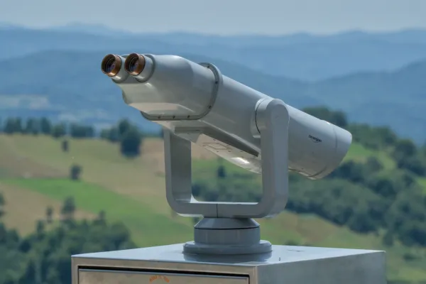 A pair of binoculars is focused on a green, rolling landscape with blue mountains in the distance.