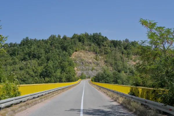 A distinctive yellow bridge with bright railings on an asphalt road in Tara National Park, Serbia, surrounded by green trees.