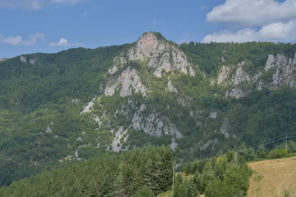Majestic Crvena Stena mountain in Serbia, with green forests and rocky slopes, viewed from a roadside cafe.