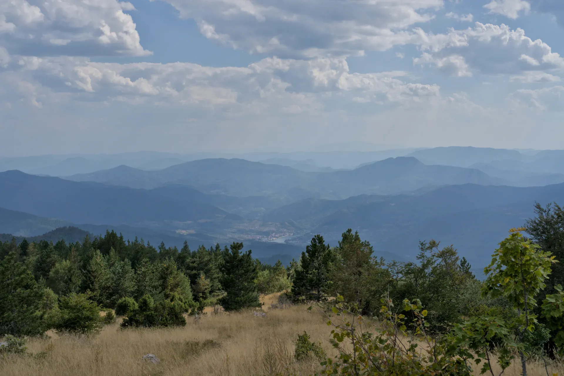 Blick auf Višegrad vom Janjač-Berg im Nationalpark Tara, Serbien, mit mehreren Ebenen blauer Berge und einem wolkigen Himmel.