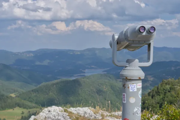A pair of binoculars positioned on a mountain peak in Tara National Park, Serbia, overlooking vast valleys and hills.