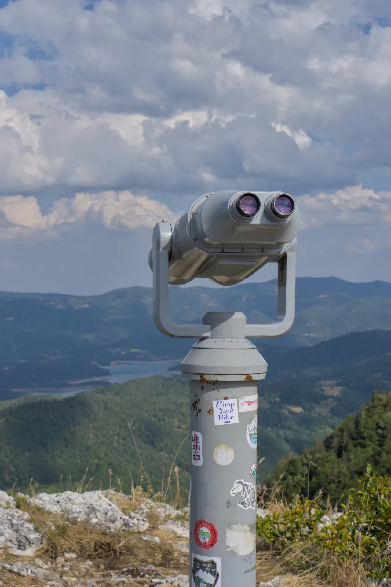 Dvogled stoji na planinskom vrhu sa pogledom na bujni, brežuljkasti pejzaž u Nacionalnom parku Tara, Srbija.