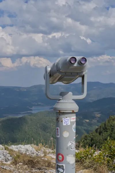 Binoculars stand on a mountain peak overlooking a lush, rolling landscape in Tara National Park, Serbia.