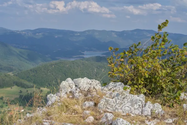Zaovine Lake seen from Jankovica mountains, Serbia, with rocks and vegetation in the foreground and rolling hills beyond.