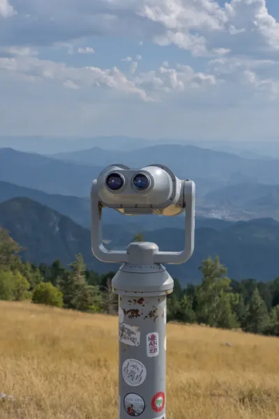 A pair of binoculars on a mountain overlooking expansive blue mountain ranges and the city of Vyšehrad.