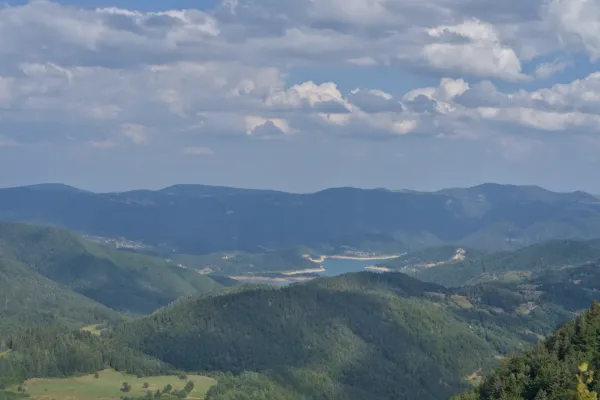 Panoramic view of Zaovine Lake from Janjač Mountain, Serbia, featuring green mountains and clouds.