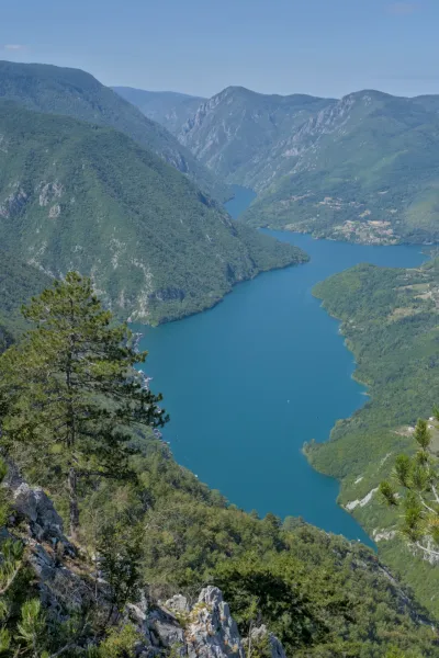 Perucac Lake viewed from the Banjska Stena peak in Serbia's Tara National Park, featuring turquoise waters and verdant mountains.