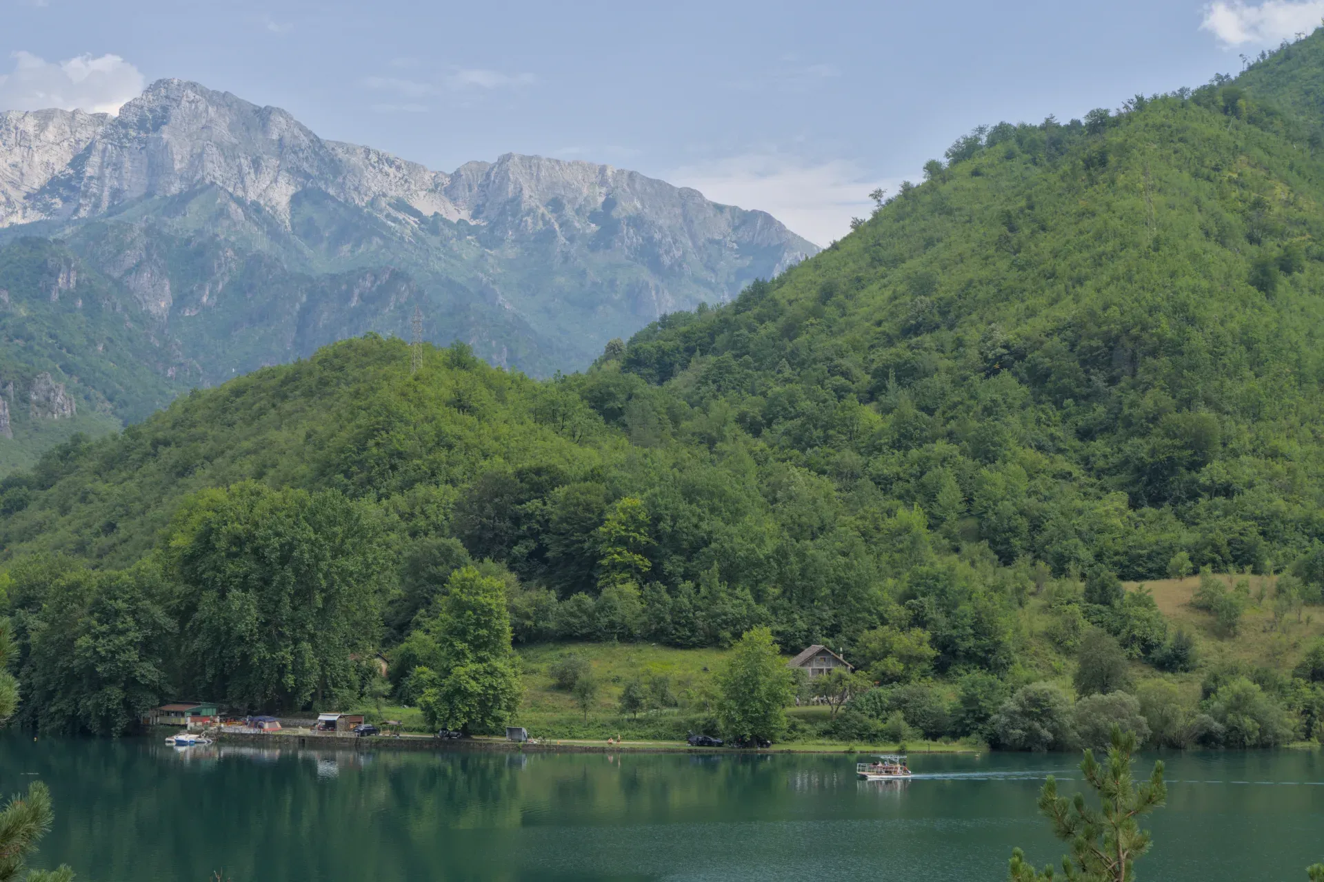 Percorso panoramico da Sarajevo a Mostar: un lago di montagna con una barca e colline verdi sotto un cielo nuvoloso.