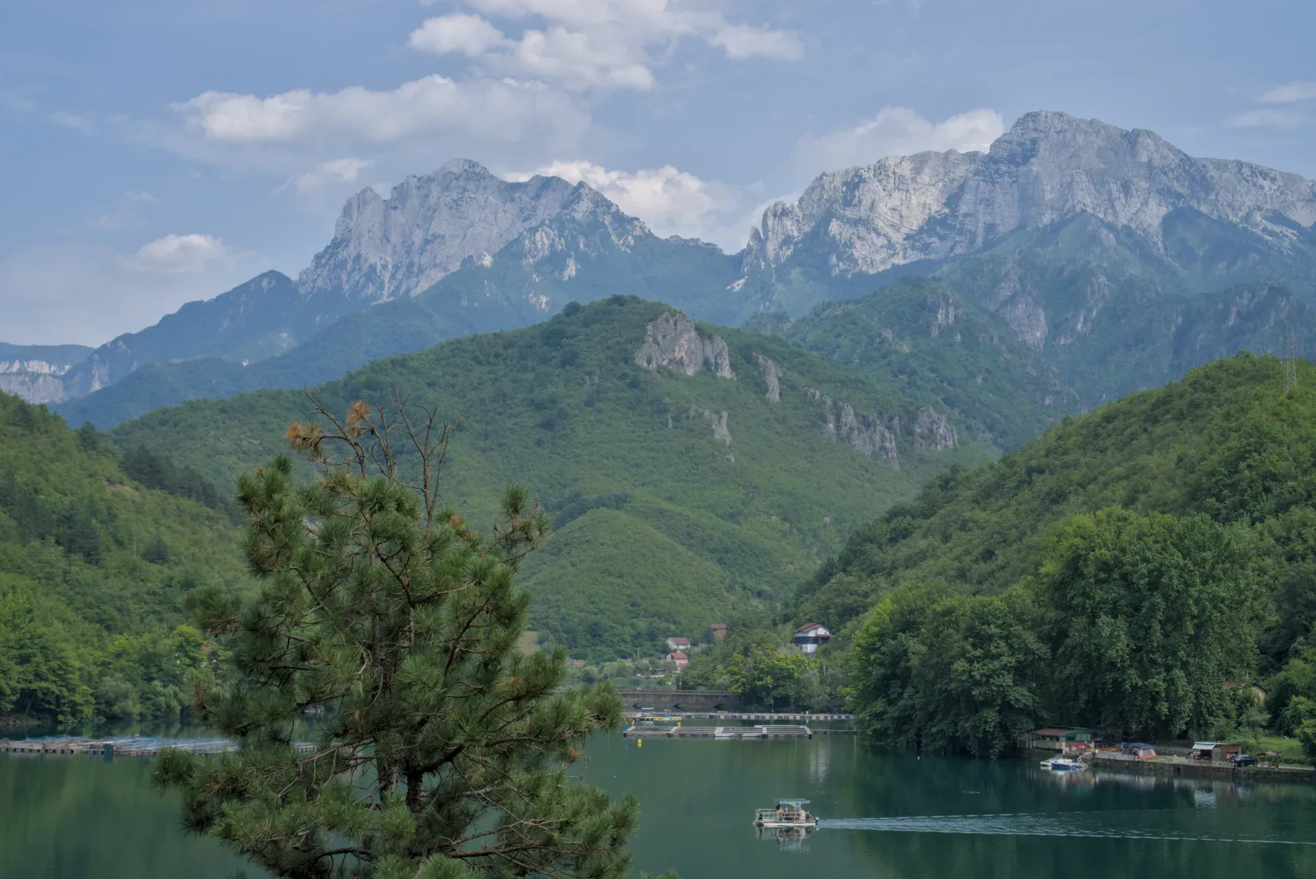 A boat travels across a beautiful lake, set against a backdrop of green mountains, on its way towards Mostar.