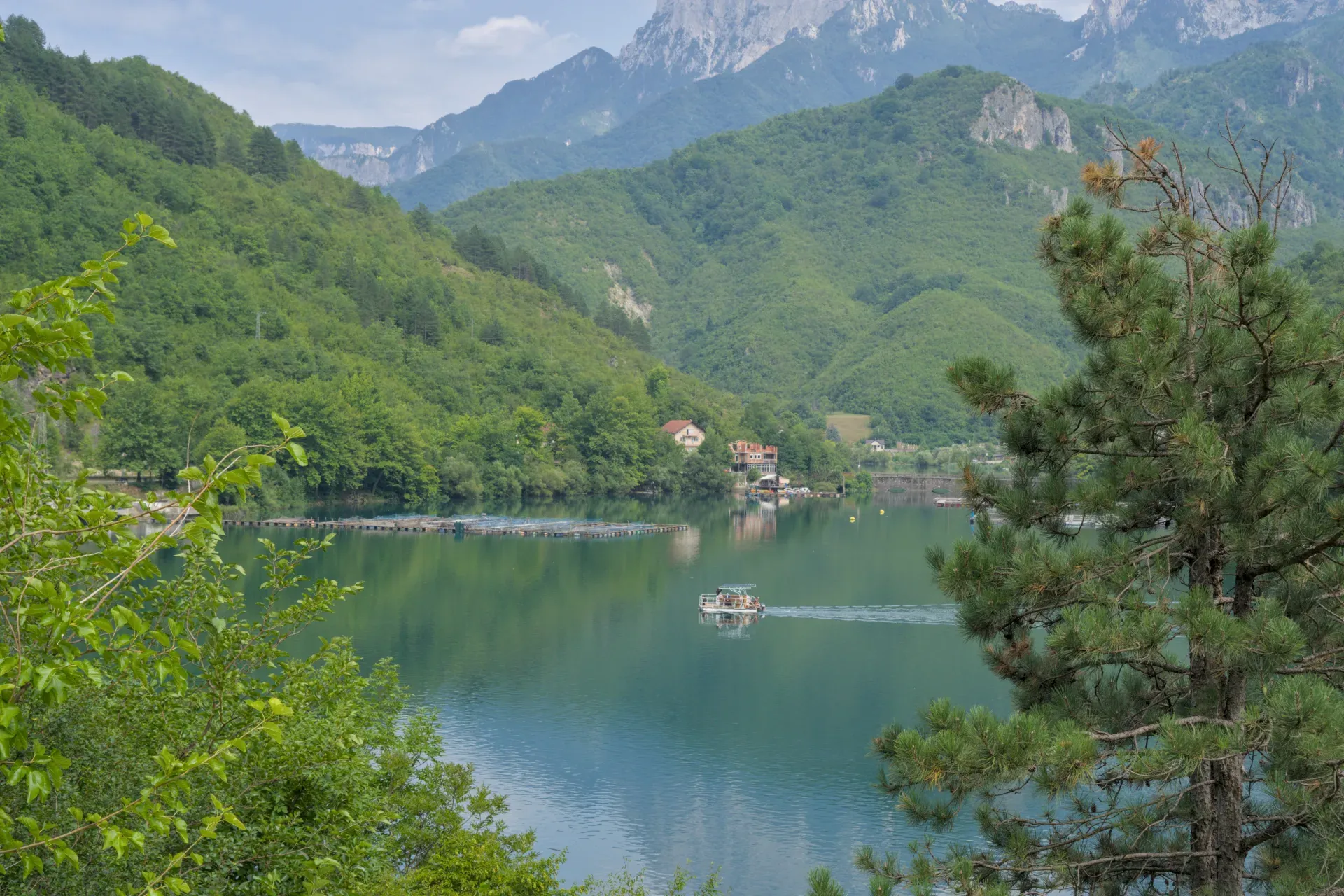 A boat glides on an azure lake with green mountains and a house by the shore, ideal for wall art.