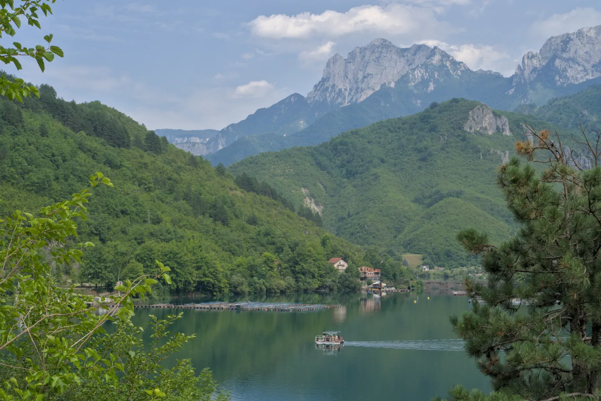 Idyllic landscape photo of a waterway towards Mostar, featuring a boat and mountains.
