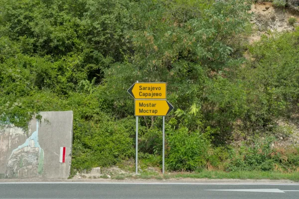 Directional sign pointing to Mostar and Sarajevo amidst lush green vegetation, marking a significant route.