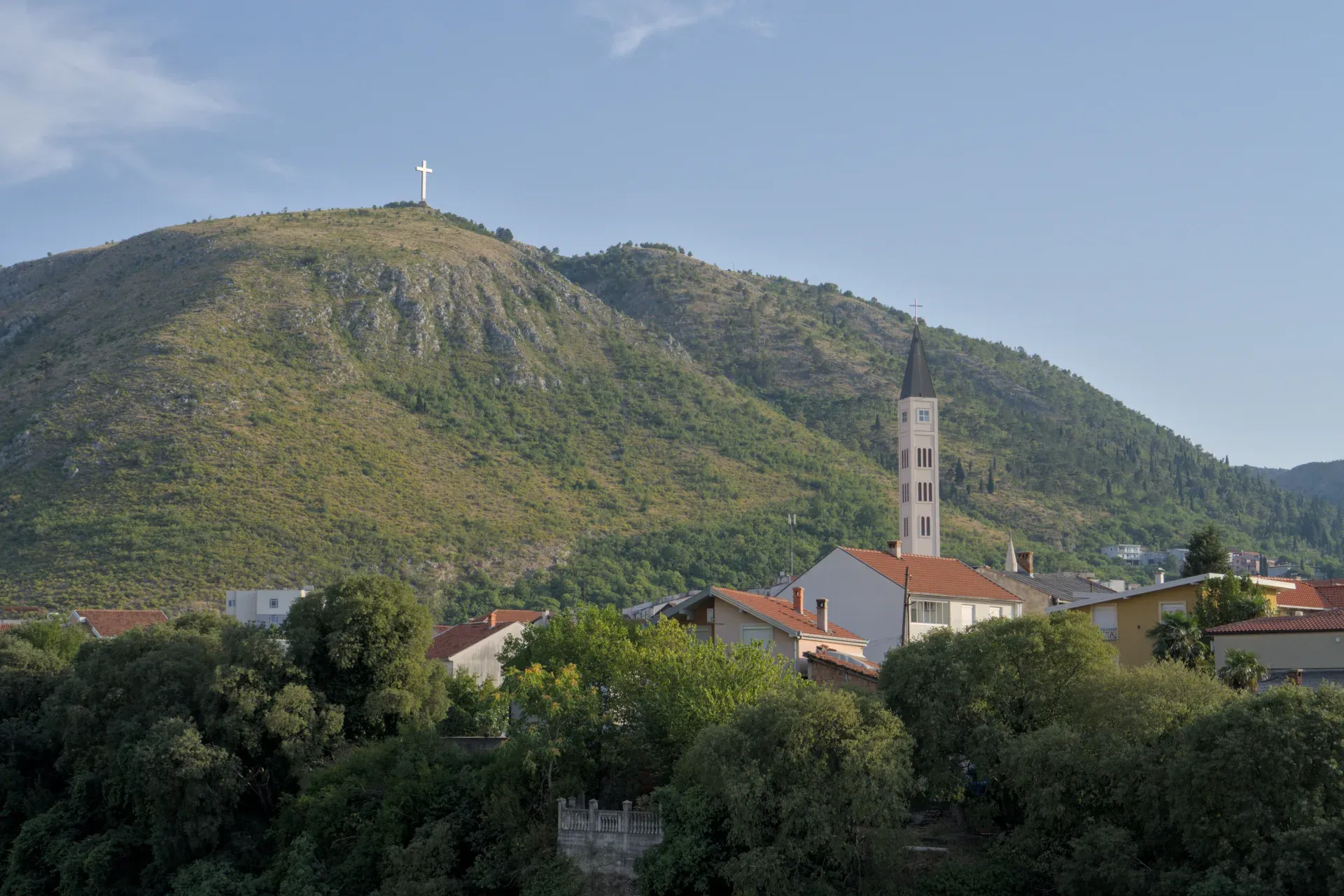 Mostar con campanario y cruz en la colina en la hora предзакатный час.