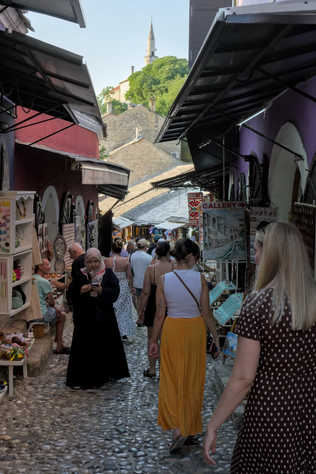 A portrait view of a bustling alley in Mostar's old town at dusk, featuring cobblestones and historic architecture.