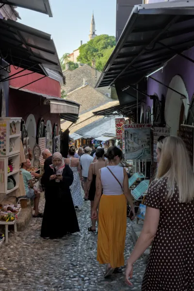 A portrait view of a bustling alley in Mostar's old town at dusk, featuring cobblestones and historic architecture.